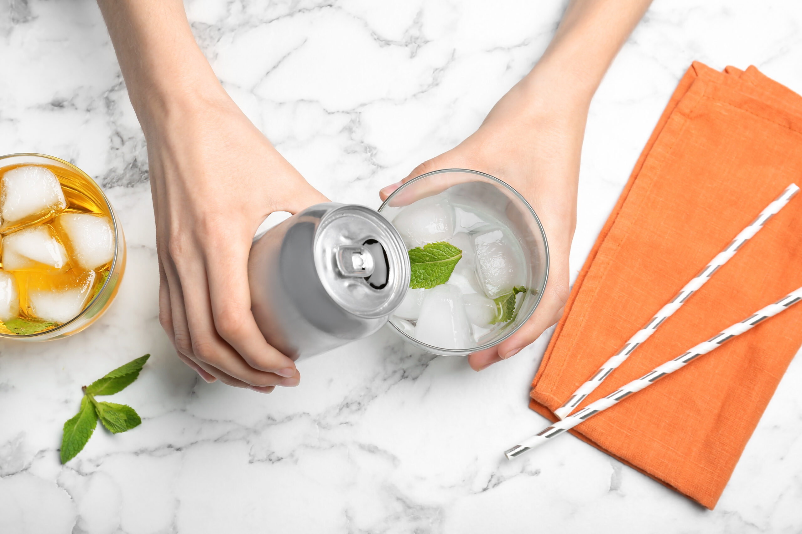 Woman pouring drink from tin can into glass at table, top view